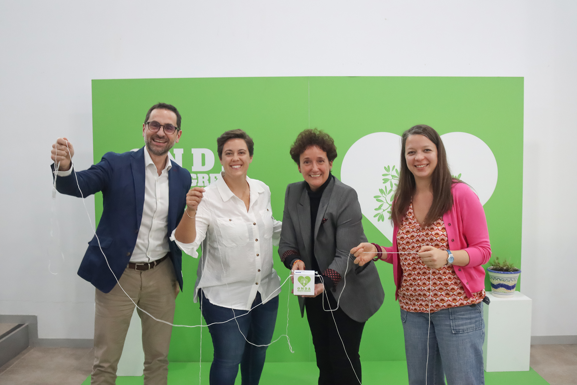 a color photo of four people smiling, holding a string in an office