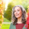 Female with curly grey hair before a red and green autumn background