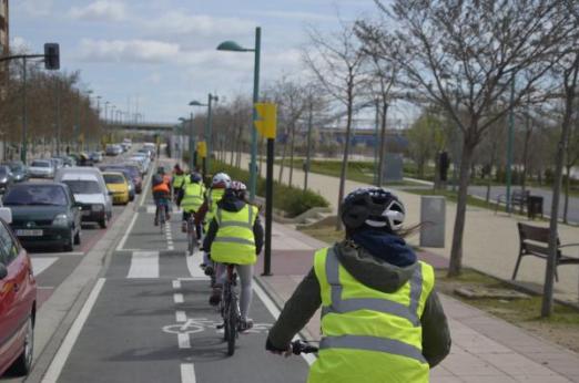 Oameni în jachete de înaltă vizibilitate, mergând cu biciclete pe o bandă dedicată pentru biciclete lângă mașini într-un ambuteiaj. Zaragoza, Spania