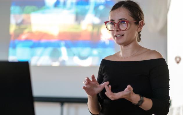 Portrait of Iris Popescu while giving a speech at a workshop. In the background there is part of the visual support.