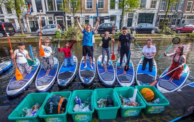  A group of people participating in a canal cleanup activity using paddleboards. 