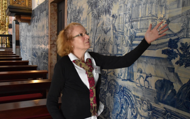 A woman indicating a painting on a wall of a building. 